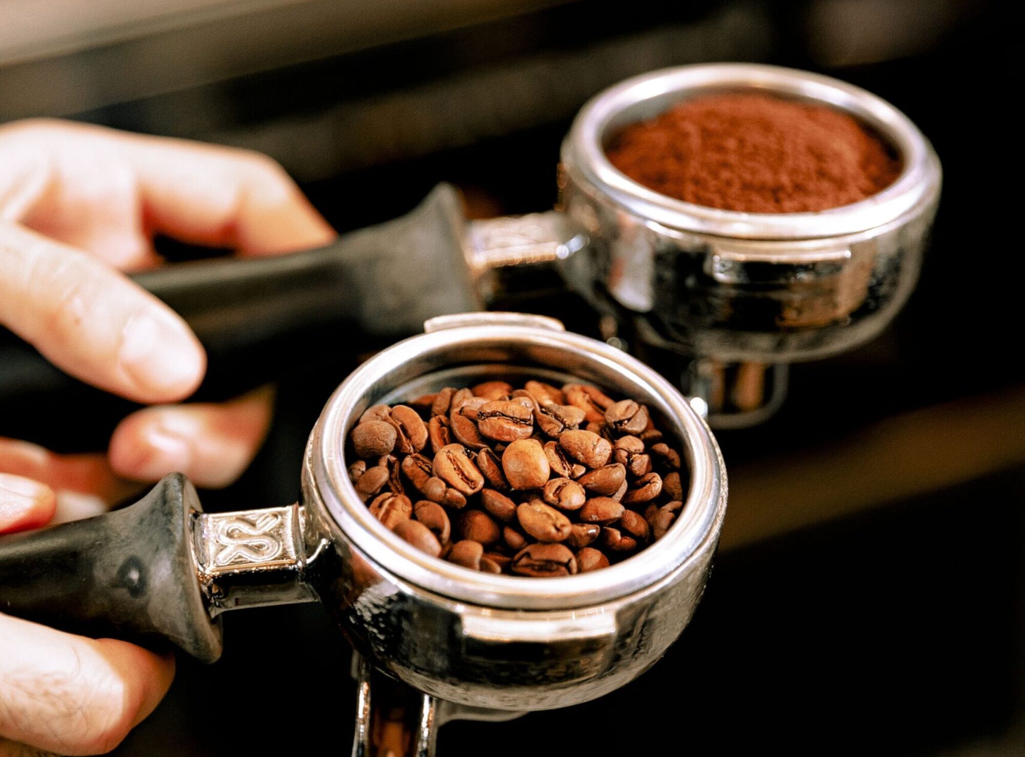 Close-up van de handen van een barista die filterdragers vasthoudt die gevuld zijn met koffiebonen en gemalen koffie.